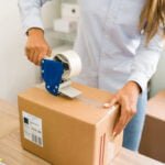 Business owner ready to ship her customers' orders. Close up of female hands putting tape on a big package with products